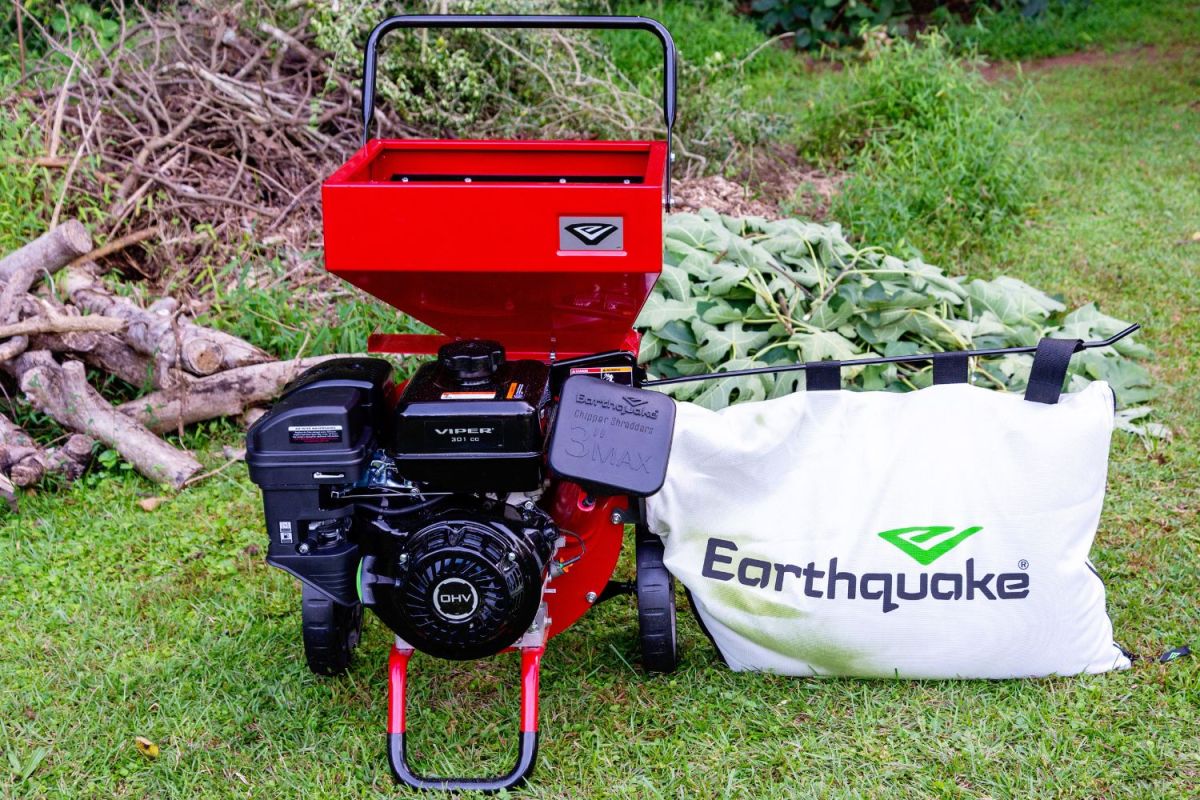 Red Earthquake K33 wood chipper on grass in front of cut logs and sticks