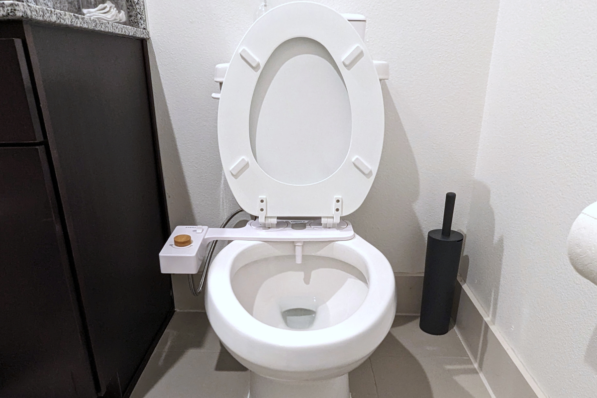 An white two-piece toilet with a Tushy Classic bidet installed with the seat and lid up in a bright bathroom.