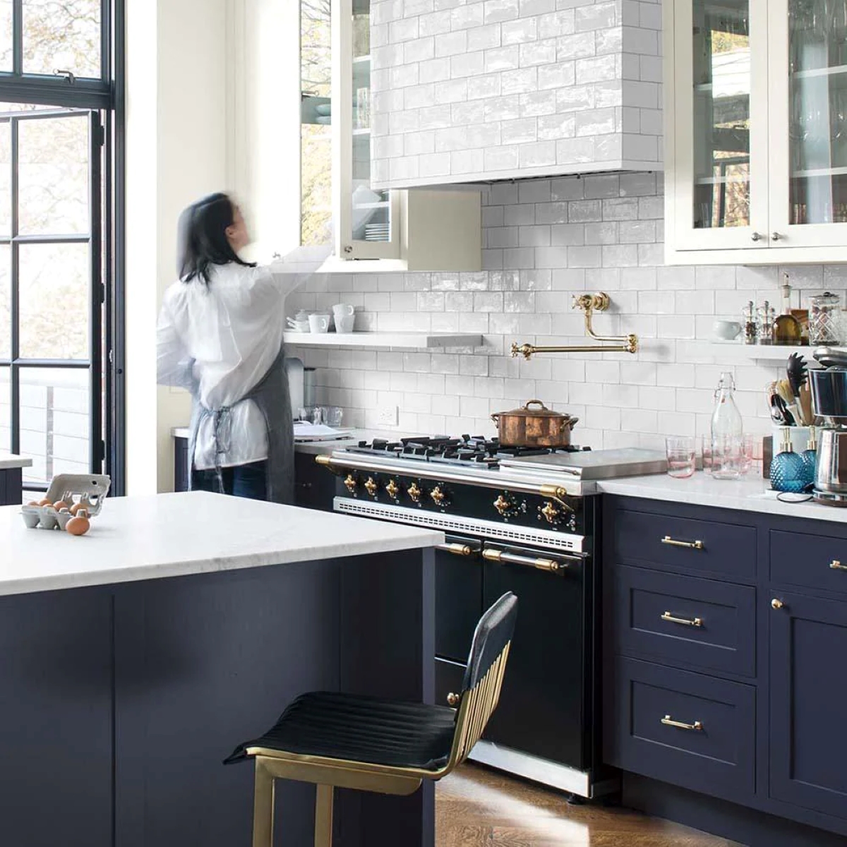 Woman in kitchen with dark blue cabinets.