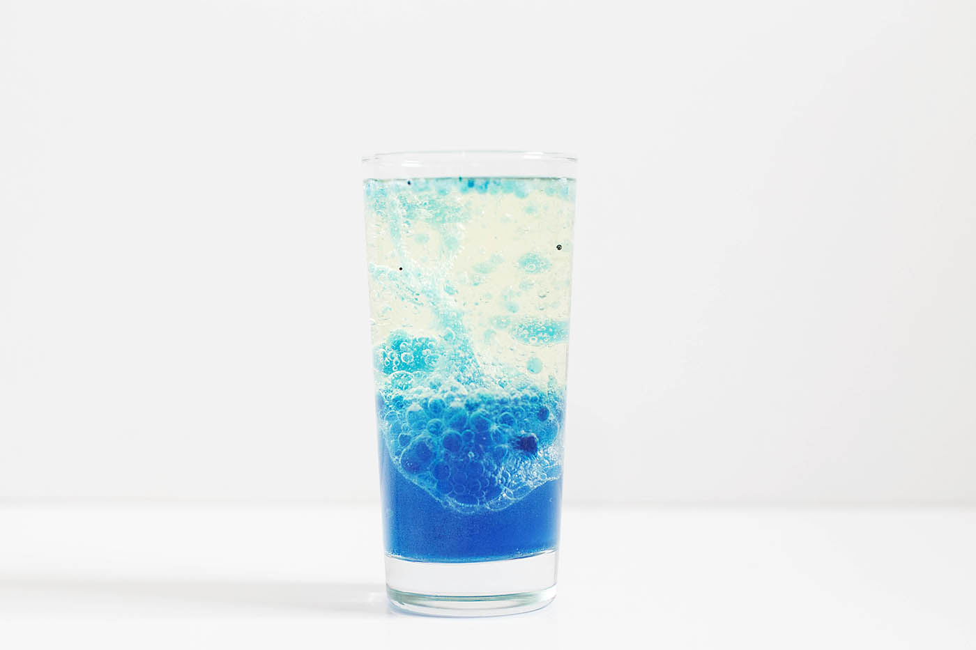 A glass against a white background with a blue homemade laval lamp inside.