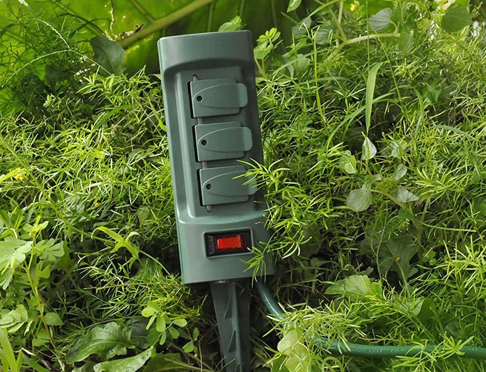 Close view of a green power stake planted in foliage near a side walk.