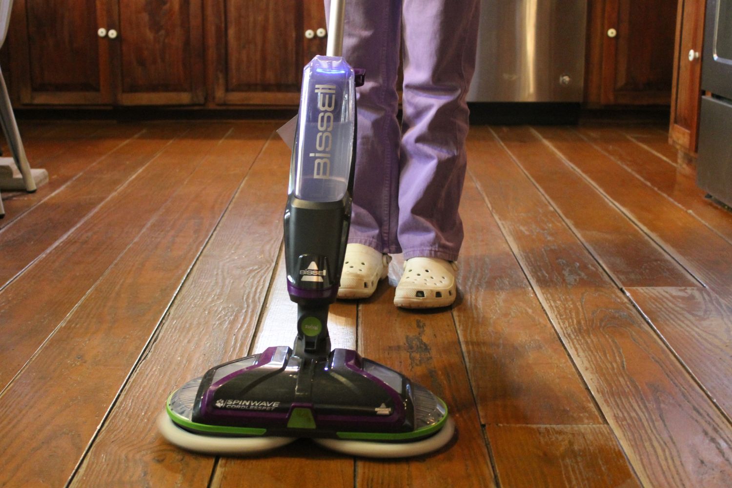 A person using the Bissell SpinWave floor scrubber to clean a wood floor.