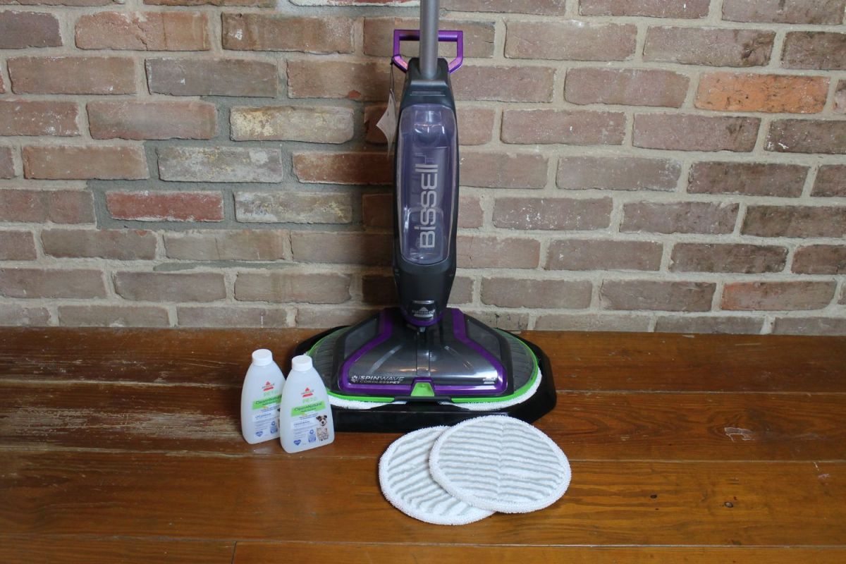 The Bisseell SpinWave floor scrubber on a wood floor with included scrubbing pads and cleaning solution.
