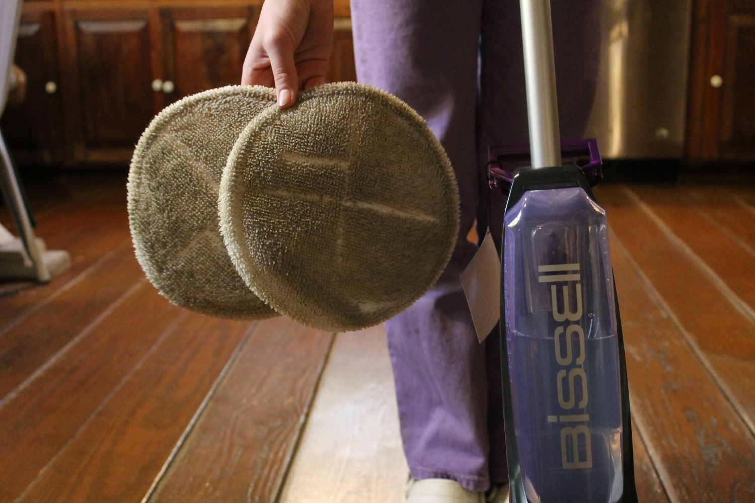 A person holding dirty floor scrubber pads after using the Bissell SpinWave floor scrubber to clean a wood floor.