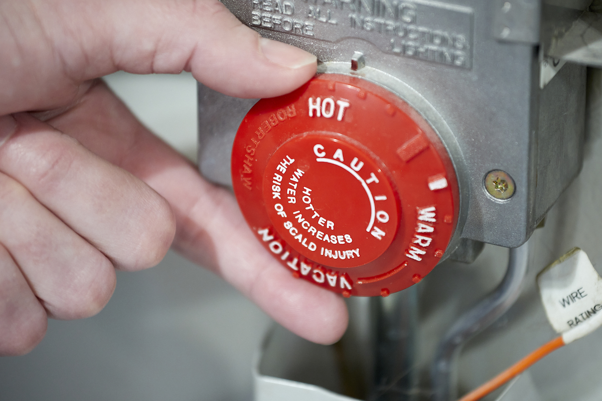 Woman adjusts the temperature on a red water heater knob.