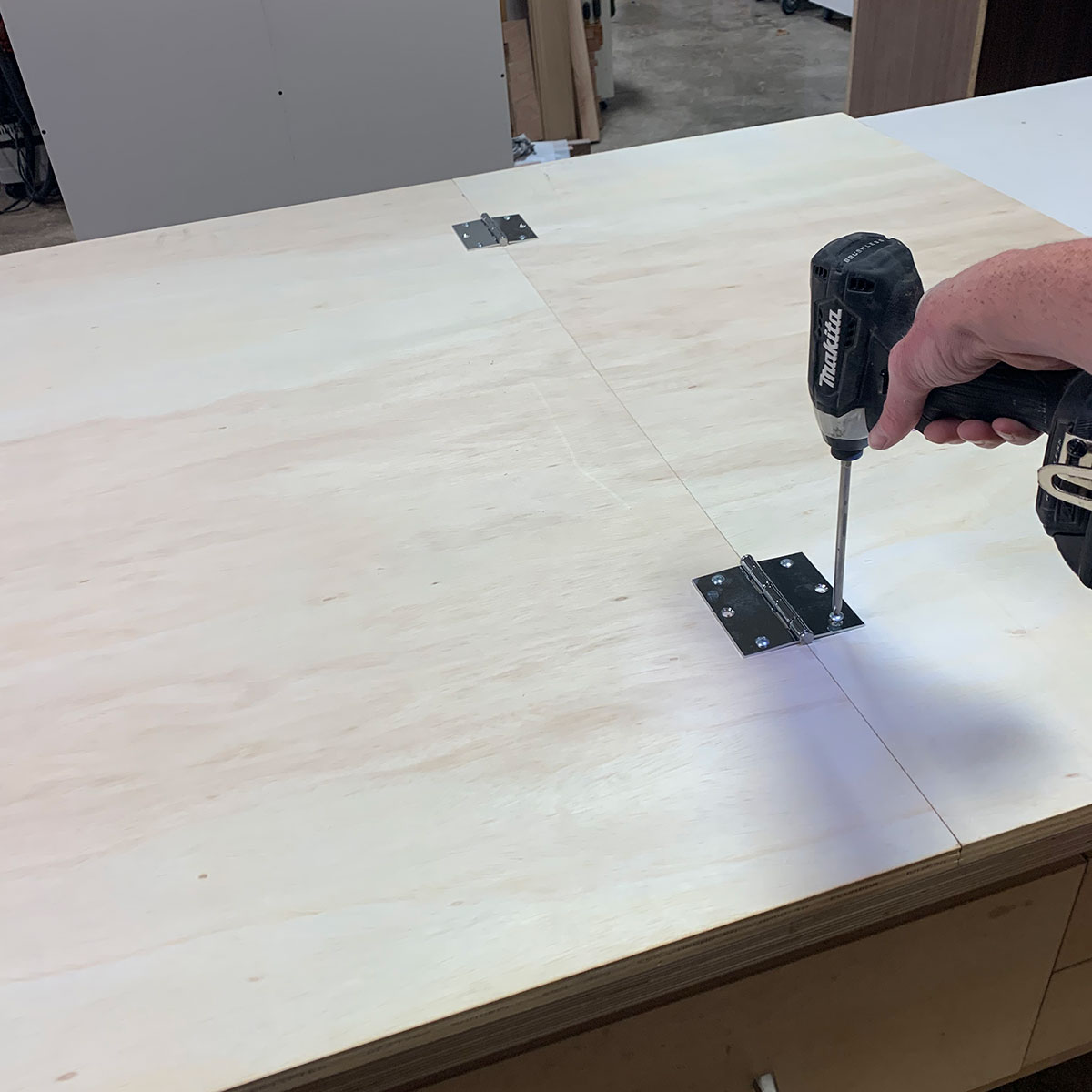 A woodworker screwing hinges on plywood to make a workbench top.