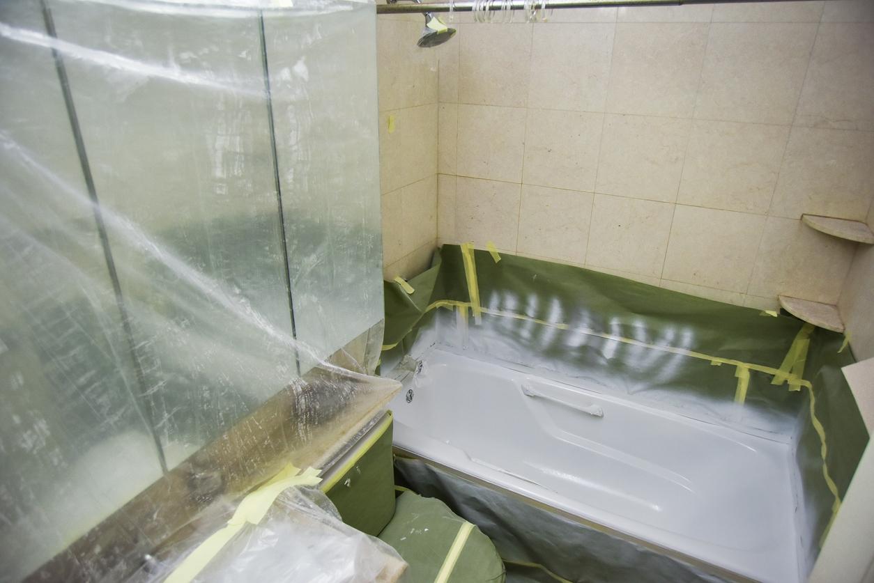 bathroom-remodel-with-plastic-tarp-over-sink-and-toilet-while-the-bathtub-is-being-repainted-white