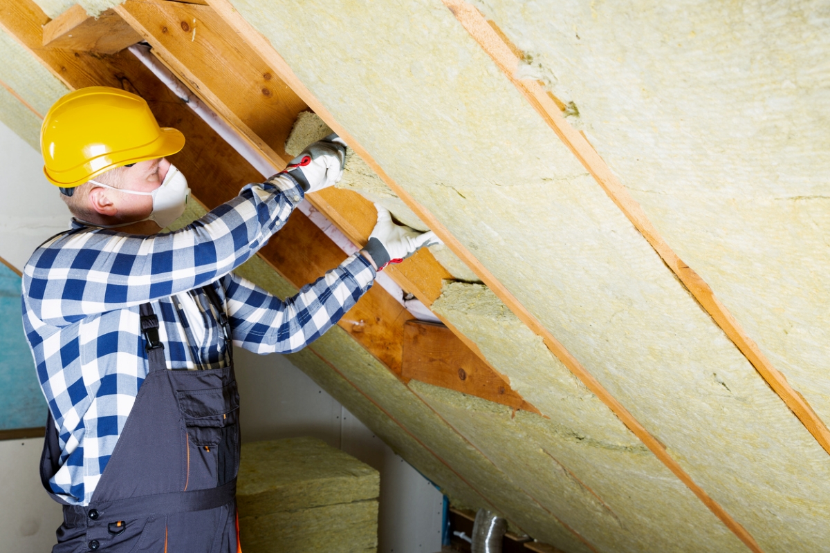 Man installing insulation in attic.