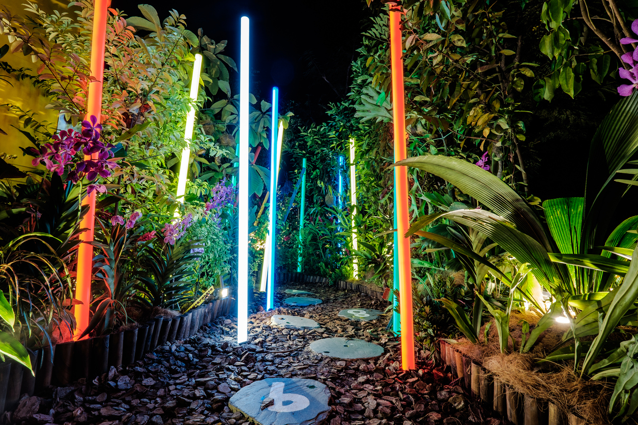 Neon-light-sticks-illuminate-a-garden-path-with-stepping-stones-and-lush-plants-on-either-side.