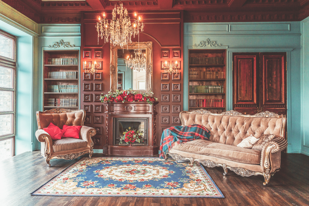 The-living-area-of-an-antique-home-with-paneled-walls-has-a-fireplace-with-floral-arrangement.