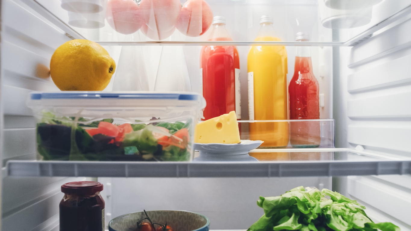 A close level view of a refrigerator shelf with a salad inside tupperware, an unwrapped piece of cheese, and juice and condiment bottles in the back.