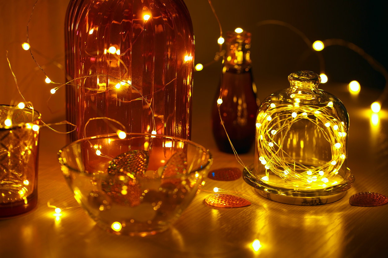 Several-glass-containers-hold-fairy-string-lights-inside-and-are-sitting-on-a-wood-table.