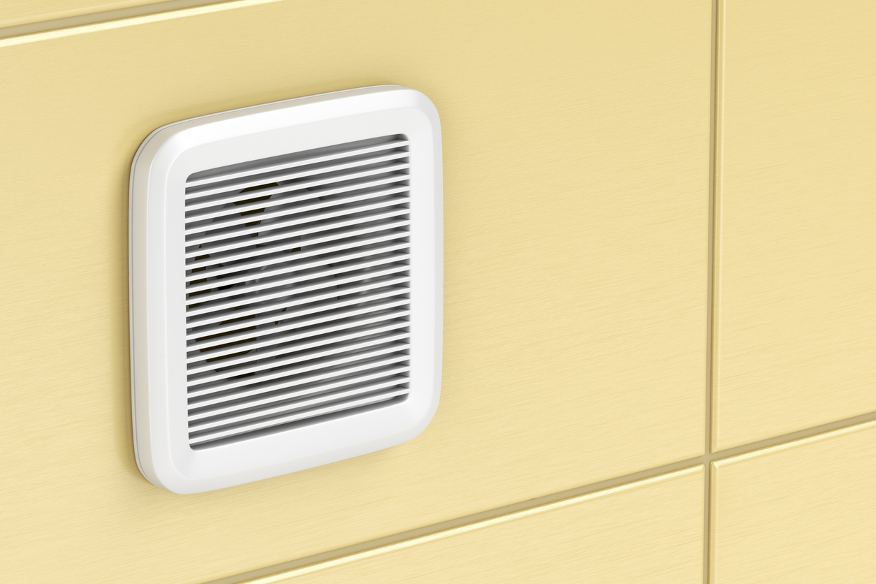 A white bathroom ventilation fan is mounted on yellow tile.