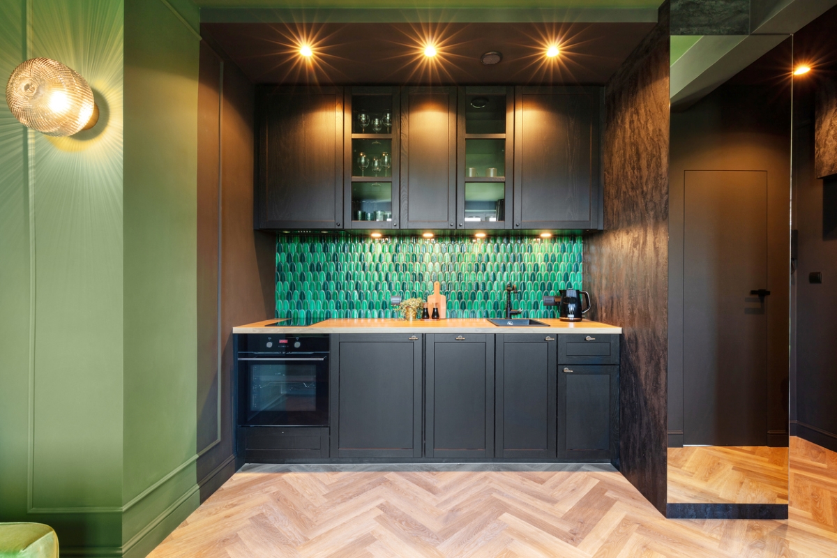 Small kitchen with green tile and black cabinets.