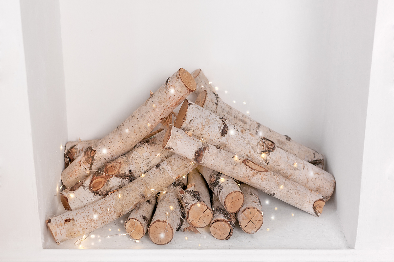 Birch-logs-in-a-white-fireplace-are-wrapped-in-fairy-string-lights.