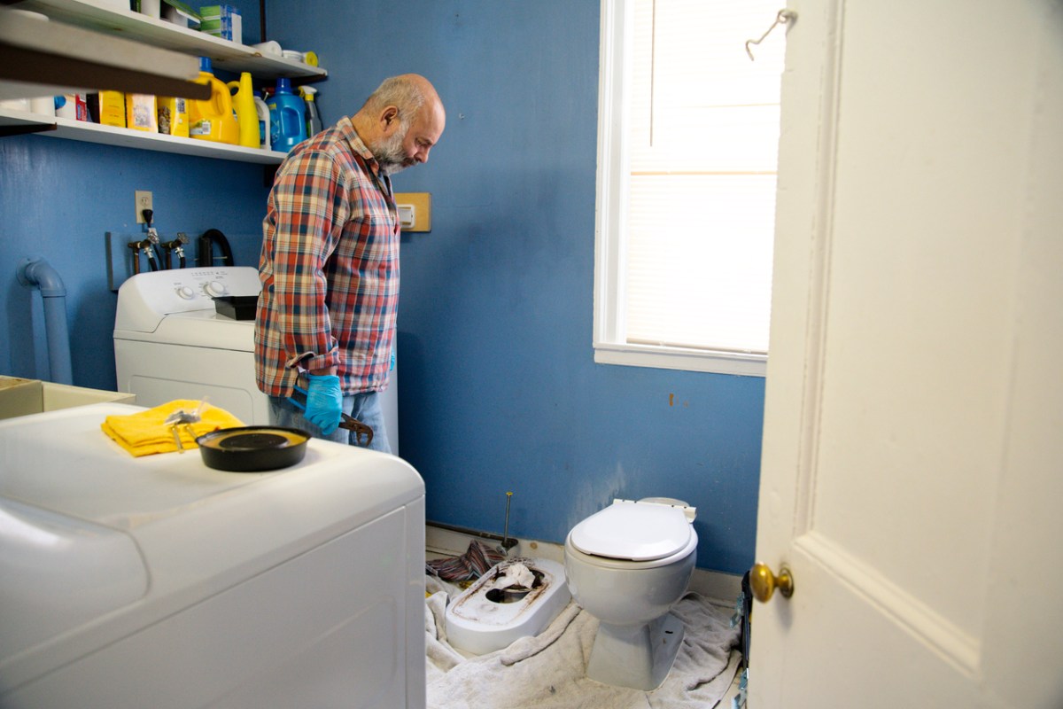A man renovating a laundry room bathroom in an old house. He is removing the toilet. Real scenario. Photographed in North America.