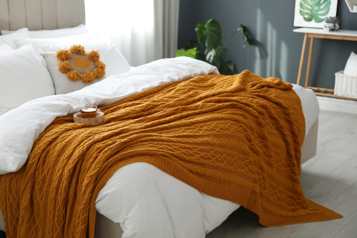 Comfortable bed with fluffy white sheets and orange knit.