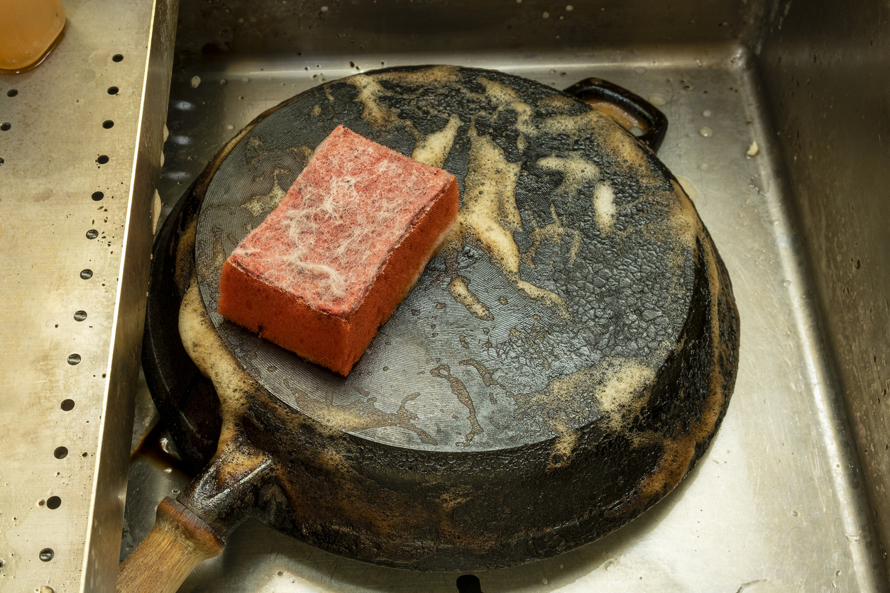 Scrubbing a cast iron skillet with a red sponge and dish soup.