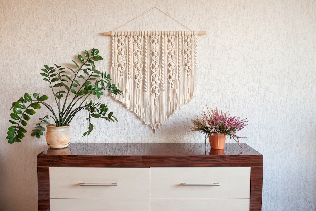 Console table in a home with potted plants and a homemade macrame project hanging on the wall.