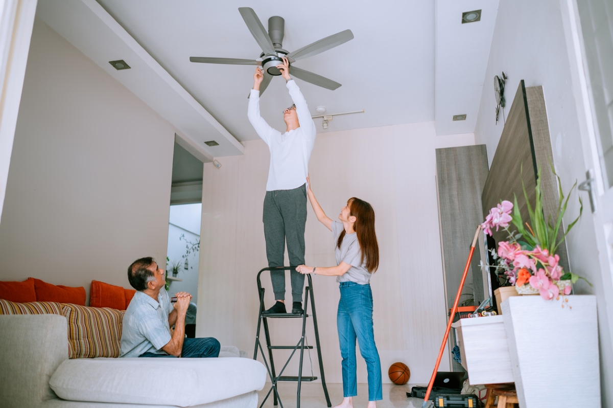 Man helping family switch ceiling fan direction on ladder.