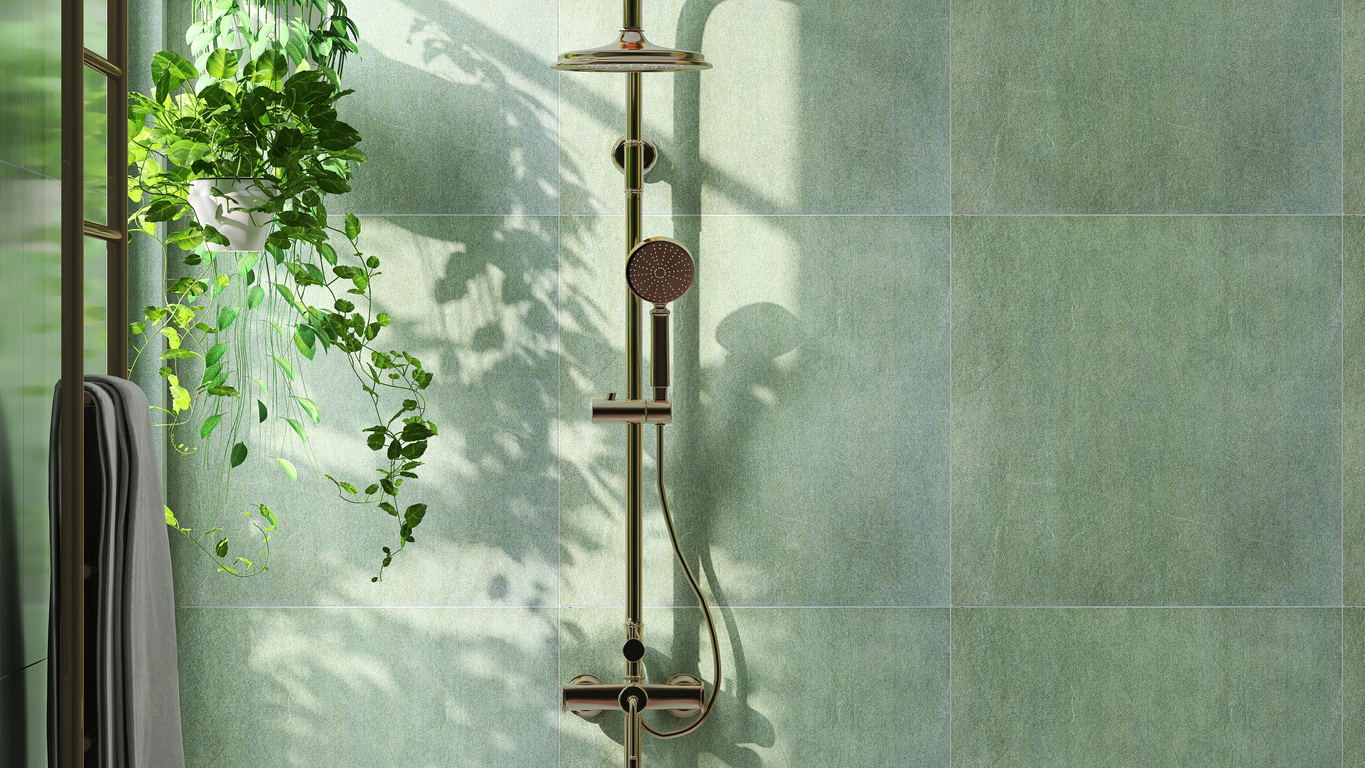 Large square sage green tiles cover the wall in a shower with a plant.