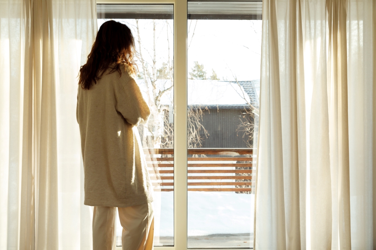 Woman standing next to open curtains.