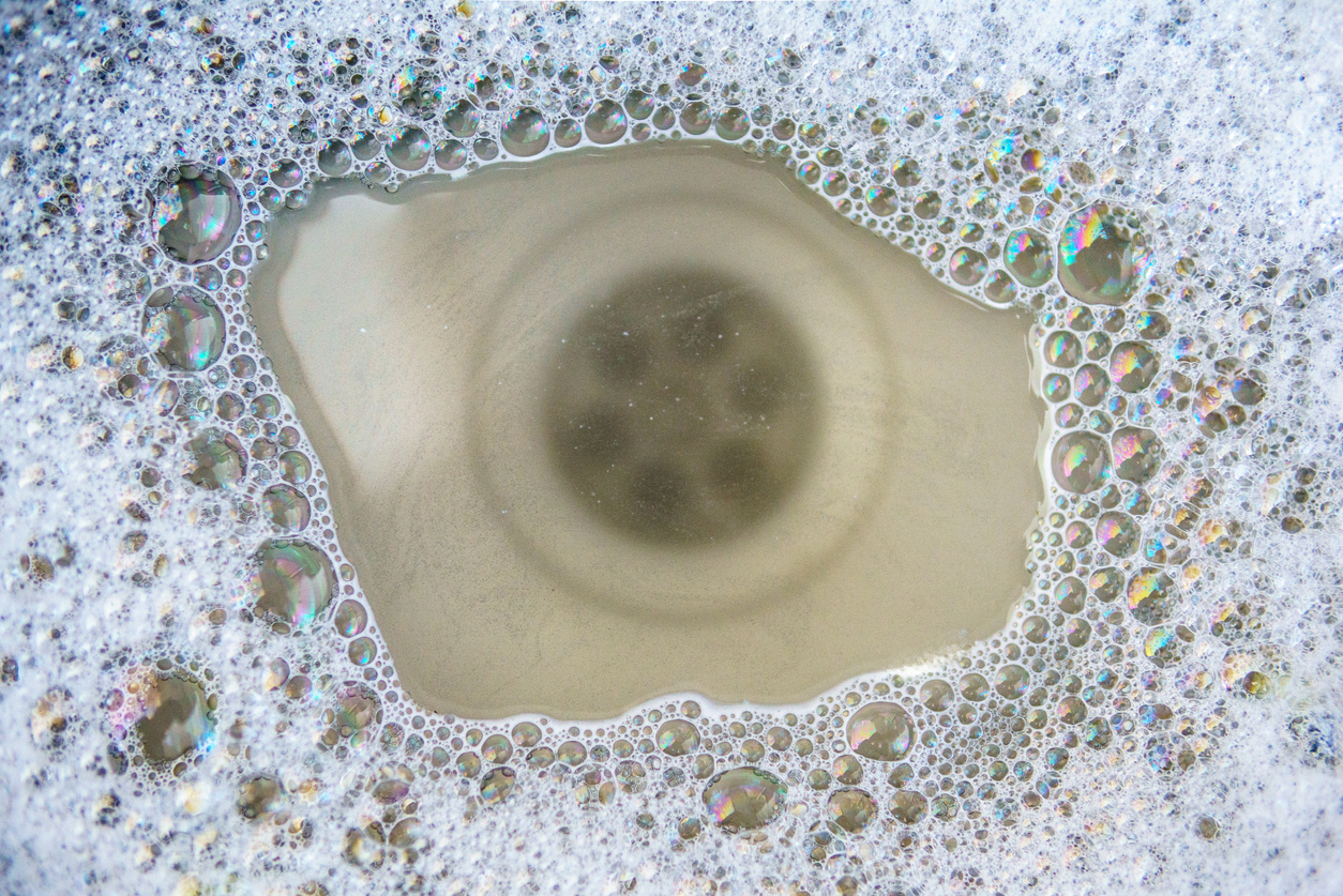 A close up view of a sink drain beneath soapy water that has built up because the drain is clogged.