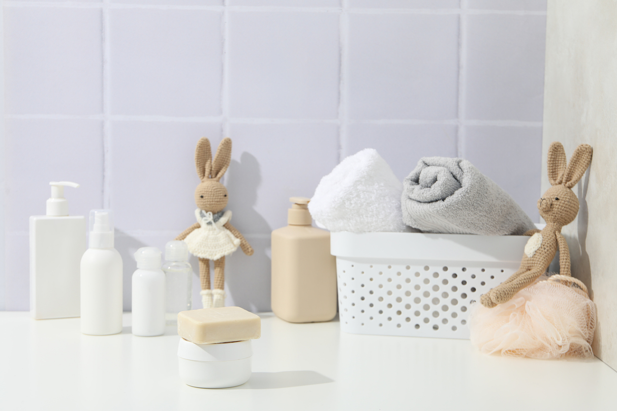 Lavender tiles have matching lavender grout on the wall of a bathroom shelf decorated with towels and rabbits.