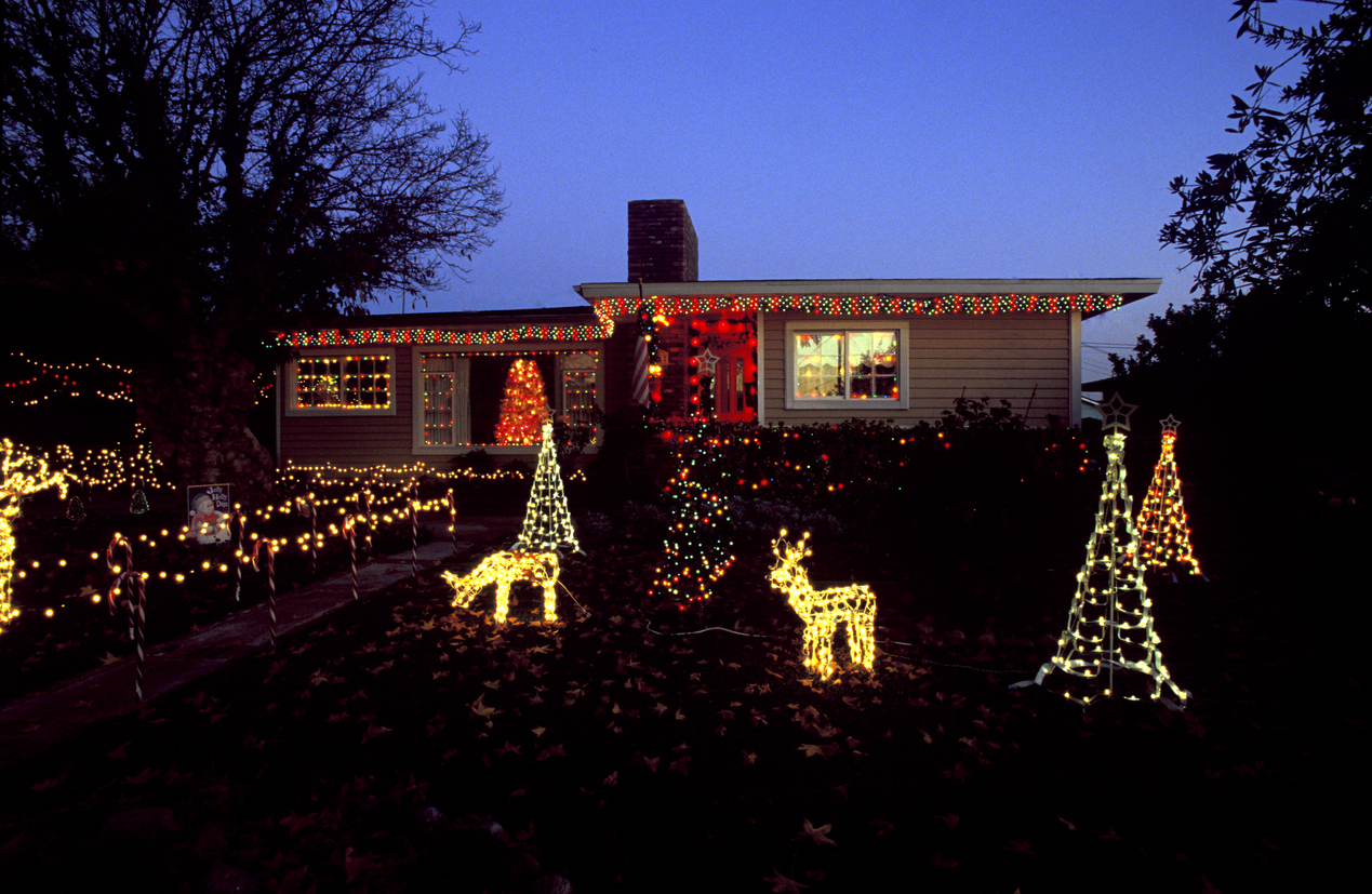 Front yard of small house with Christmas decorations in front yard at twlight, with reindder and tree lights.