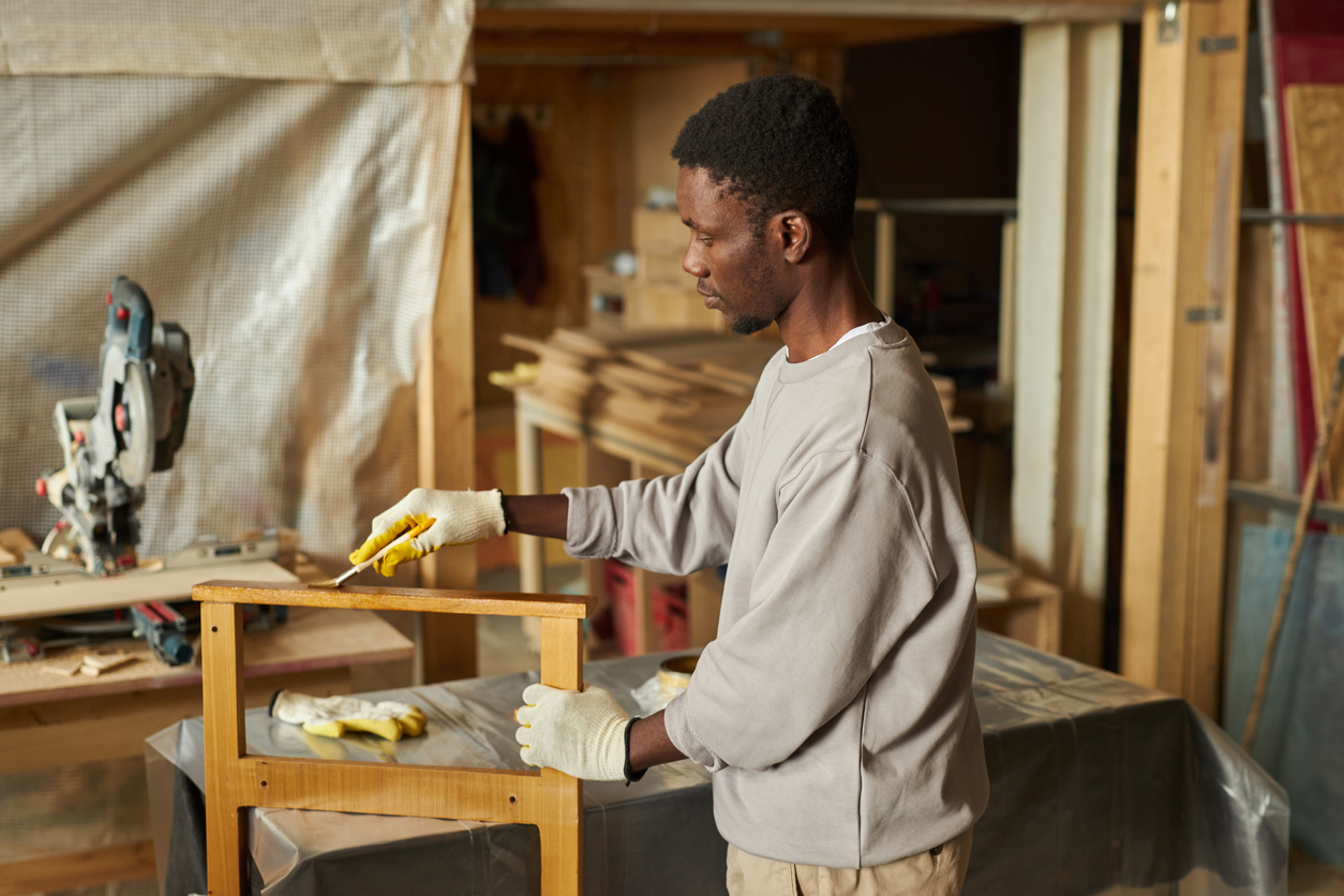 Side view portrait of young African American man refinishing wooden furniture in workshop