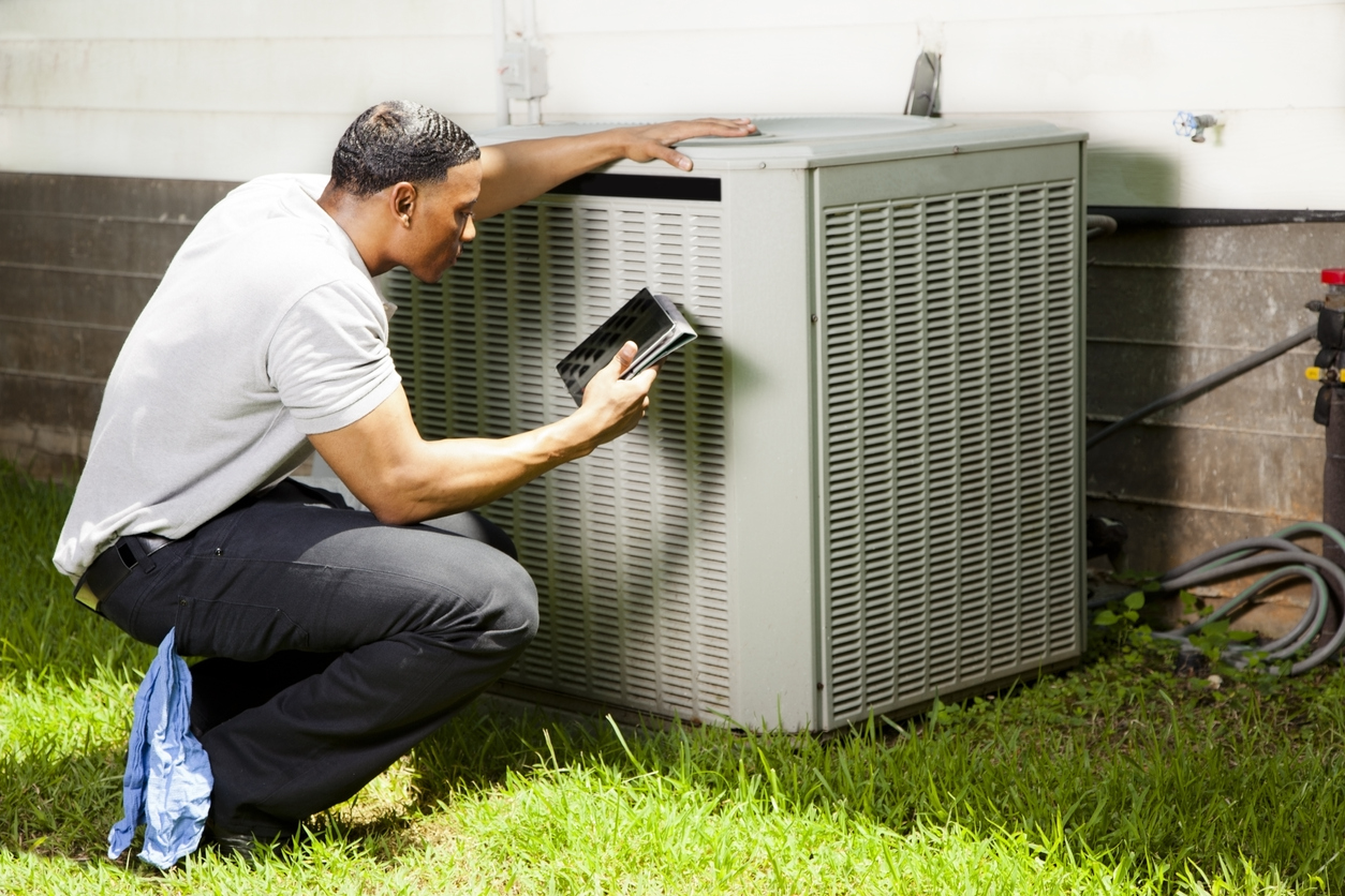 A-repair-person-uses-a-tablet-to-get-readings-on-an-HVAC-unit-outside-of-a-home.