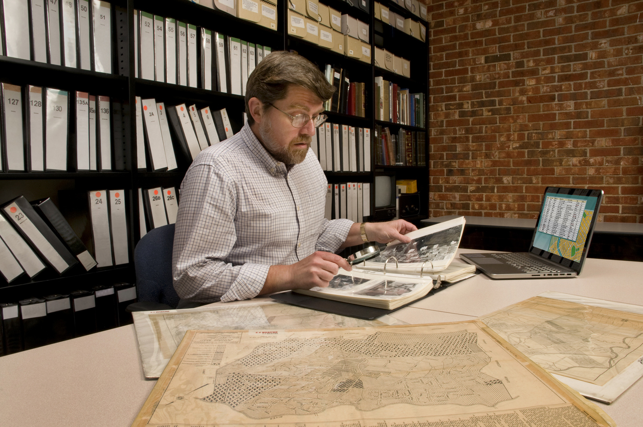 Researcher in archive, searching through maps and photographs.