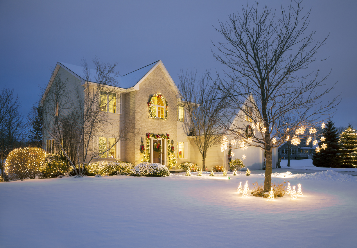 A white brick house decorated with white christmas lights and a large lawn covered in snow.