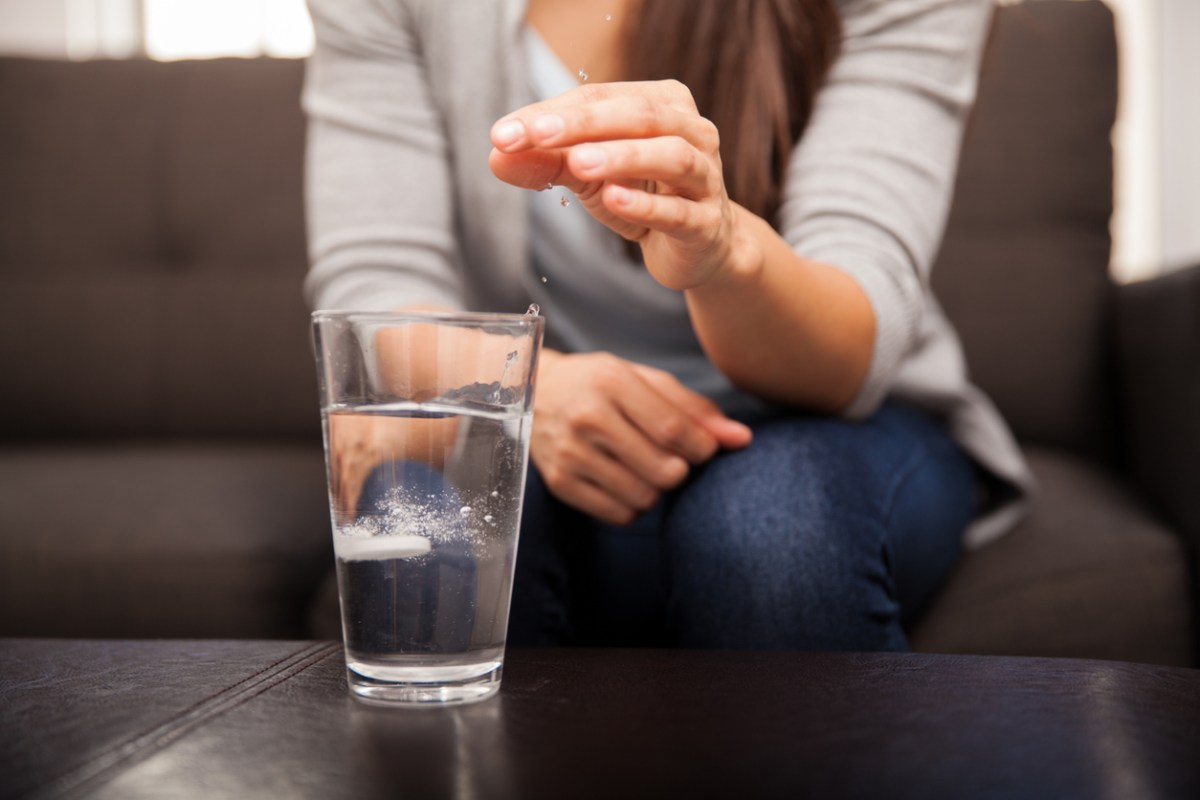 Closeup of a young woman dropping an effervescent antacid in a glass of water.