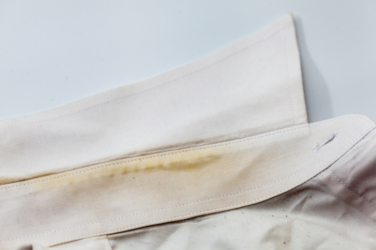 A close view of a white shirt collar with yellow and green stains on it.