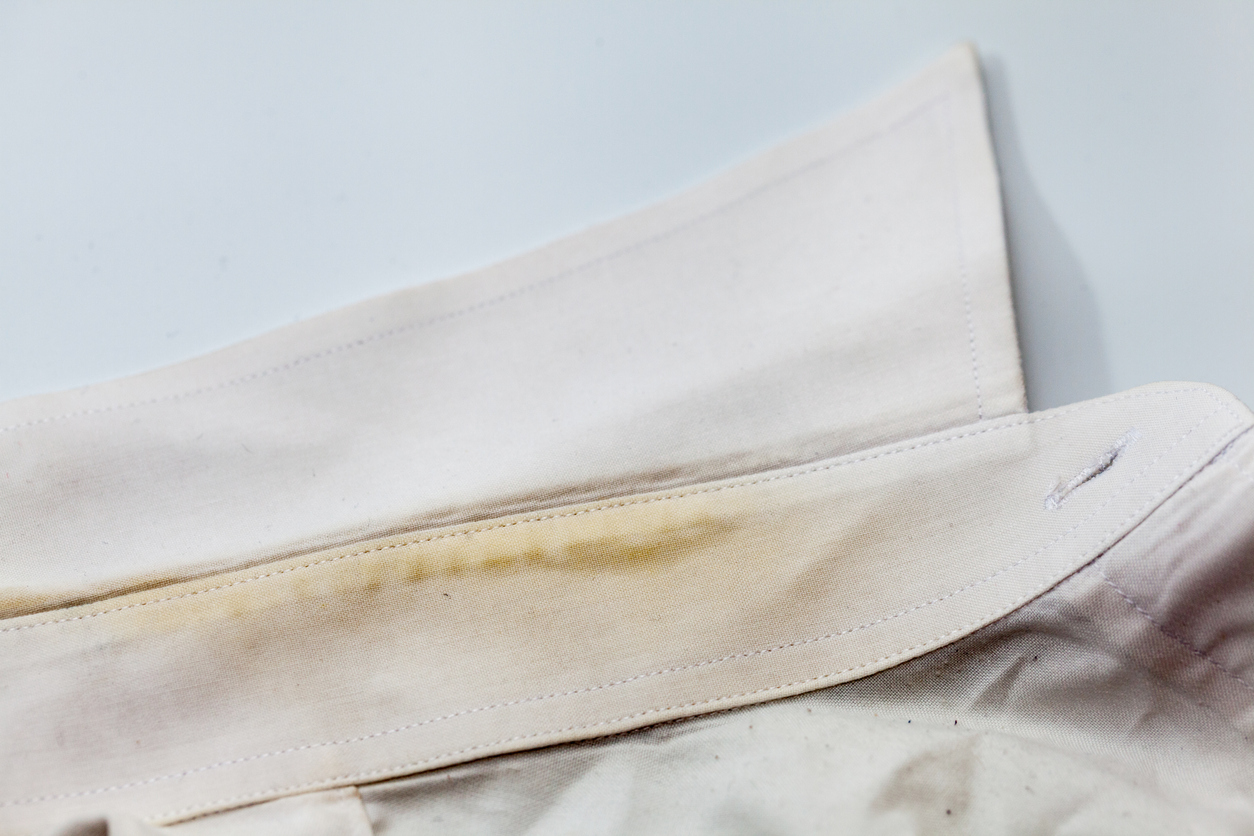 A close view of a white shirt collar with yellow and green stains on it.
