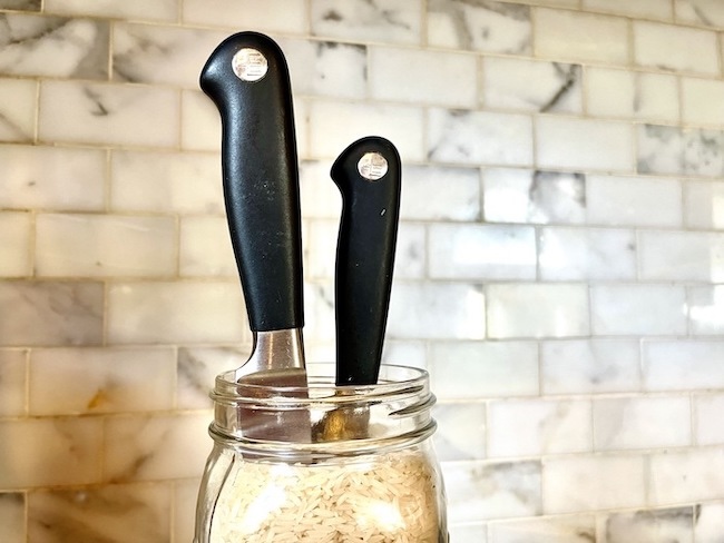 Two black-handled knives stored in a rice-filled Mason Jar