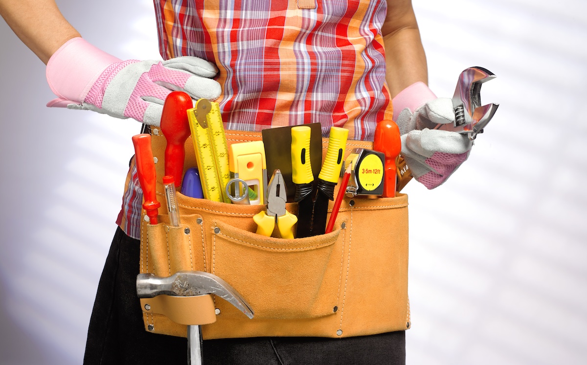 Lower half of a woman wearing a tool belt and holding a wrench.