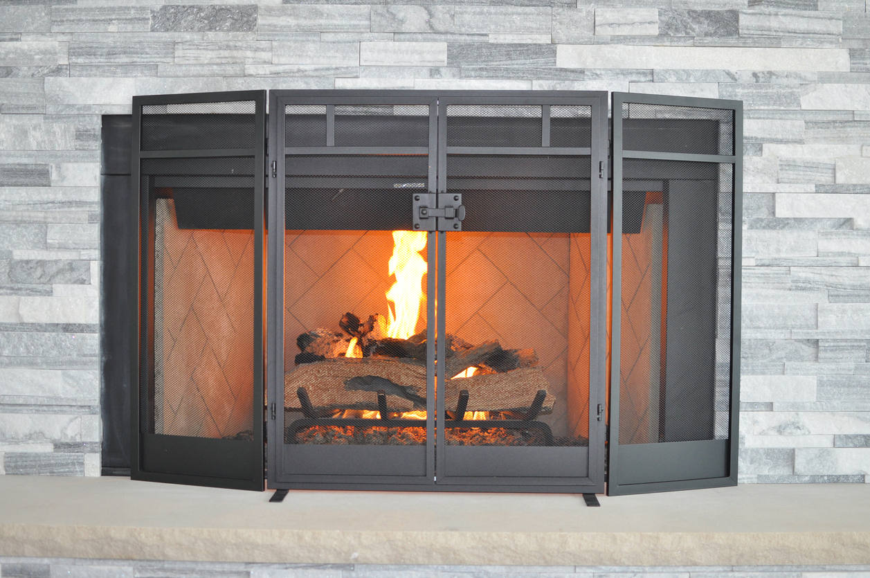 The best fireplace screen shielding a grey stone hearth from a burning fire.