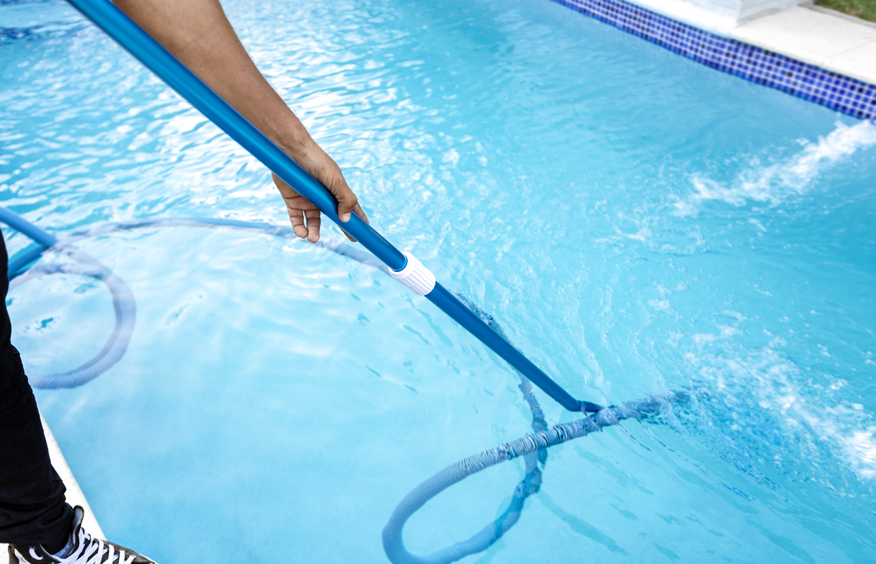 A person cleaning a pool using the best handheld vacuum on an extender pole with a hose attached.