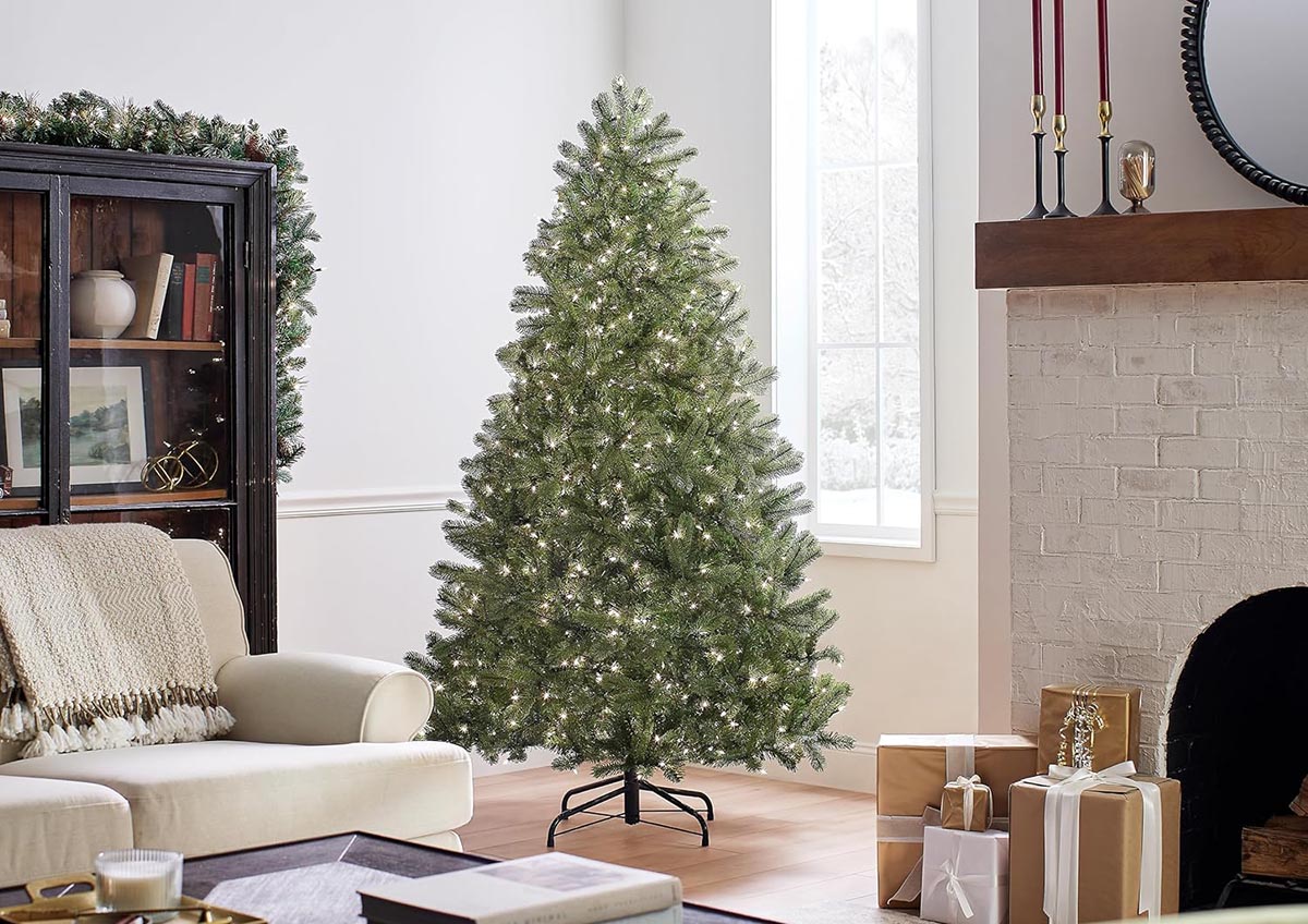 The National Tree Company Full Downswept Christmas Tree in a neutral living room next to a brick fireplace with wrapped presents.