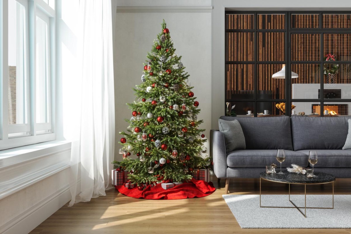 The best Christmas tree under $300 with red and white ornaments and a red tree skirt next to a window and grey couch.