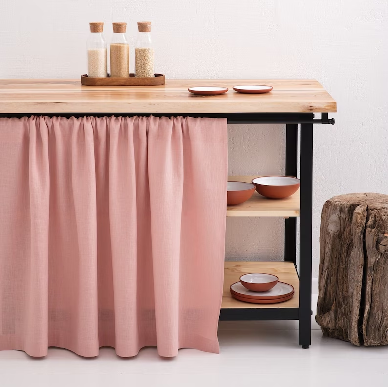 A small kitchen side table covered with a pink curtain.