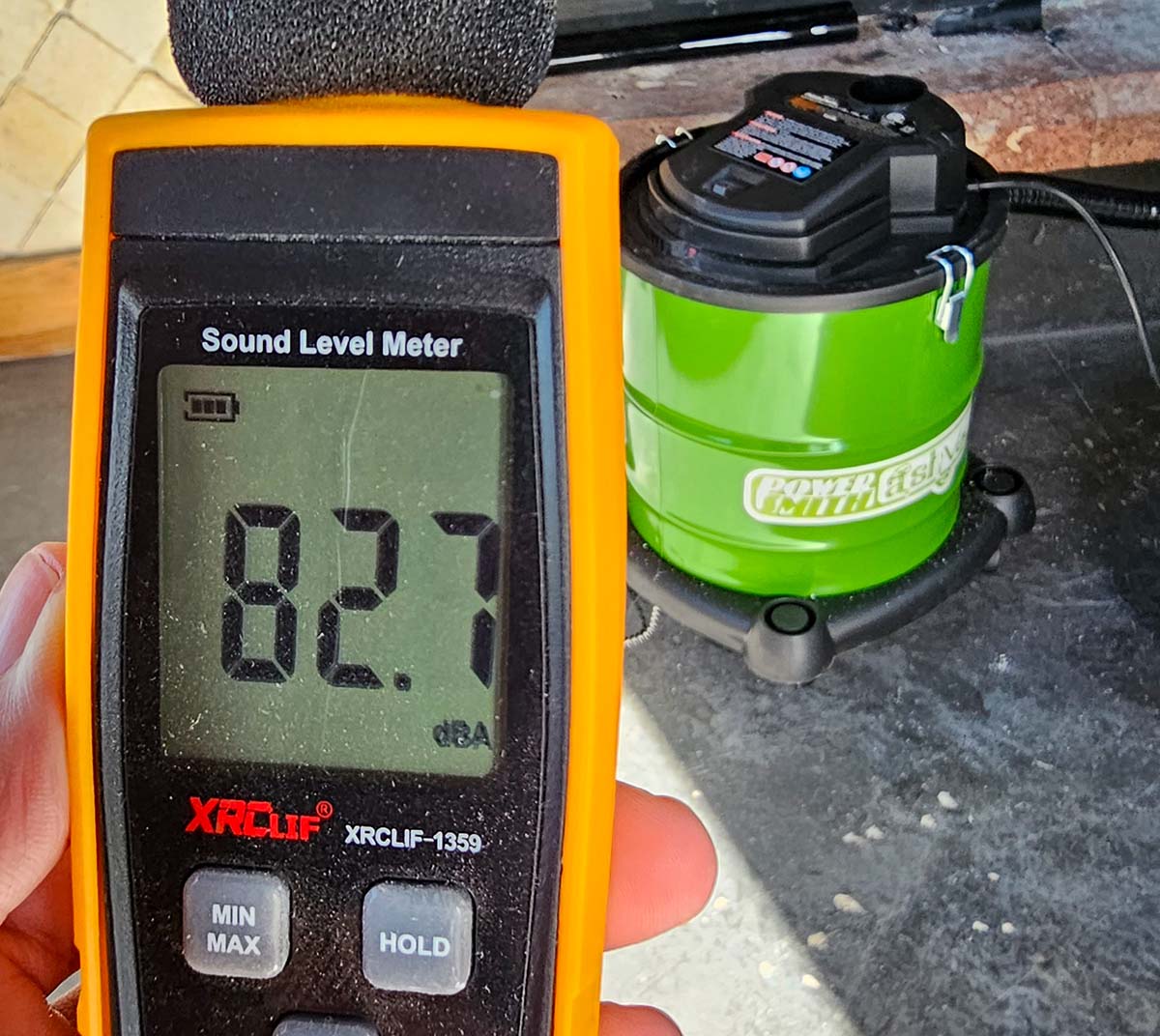 A decibel meter showing a reading of 82.7 with the PowerSmith ash vacuum in the background.