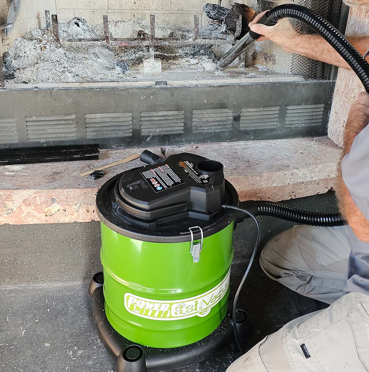 A person using the PowerSmith ash vacuum to clean a firebox.