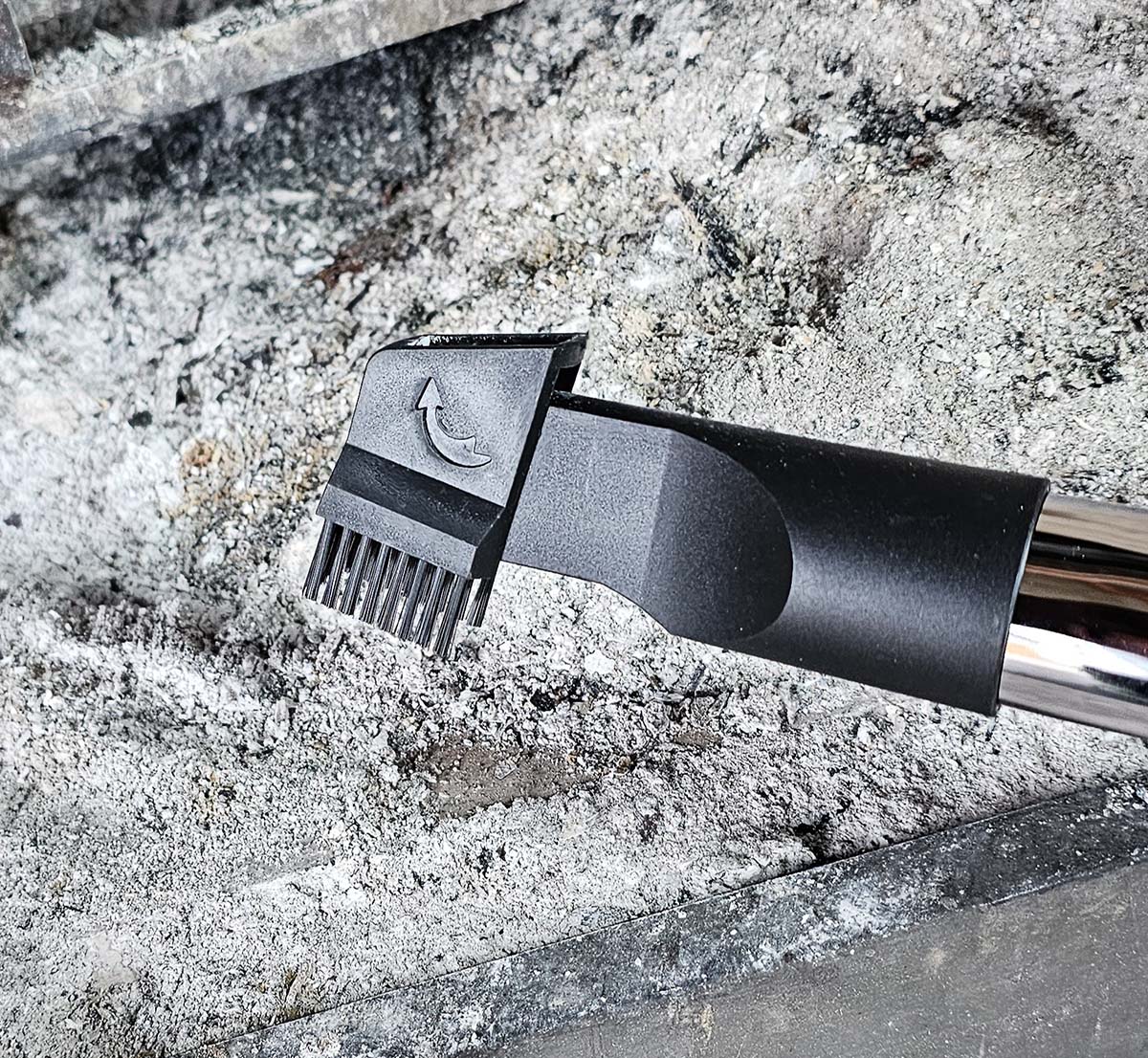 The brush attachment of the PowerSmith ash vacuum in front of a pile of ashes in a firebox.