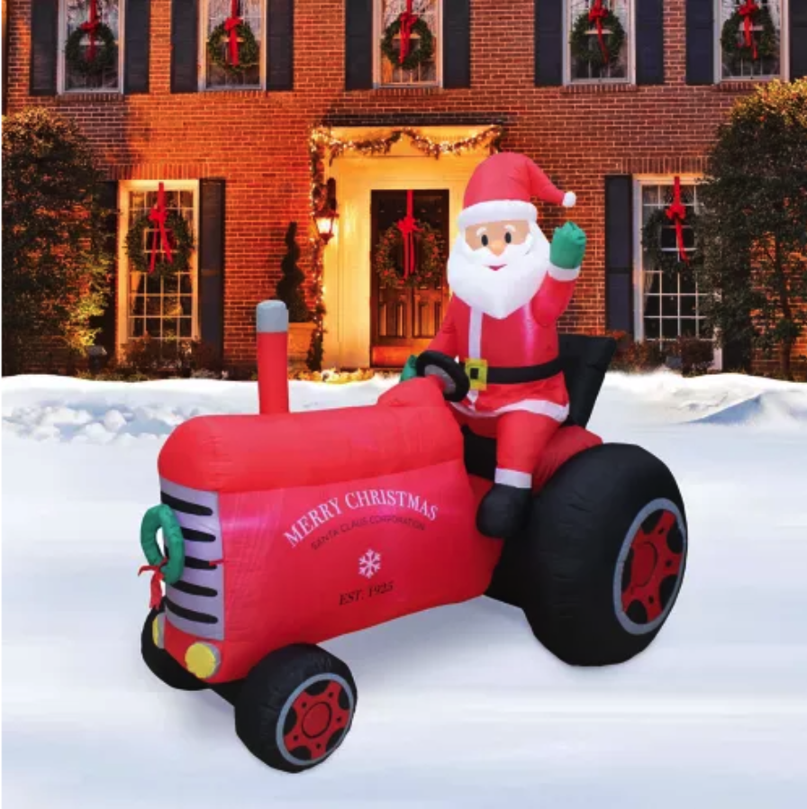 Large santa inflatable riding an old tractor in front of a home