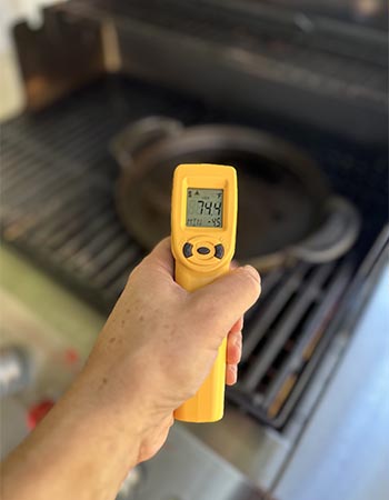 Person taking interior temperature of grill with a yellow Thermoworks IR gun