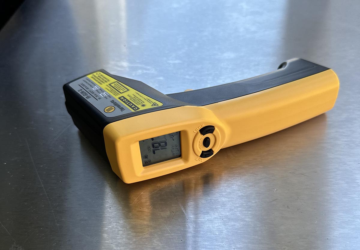 Yellow and black ThermoWorks IR Gun on its side on stainless steel countertop