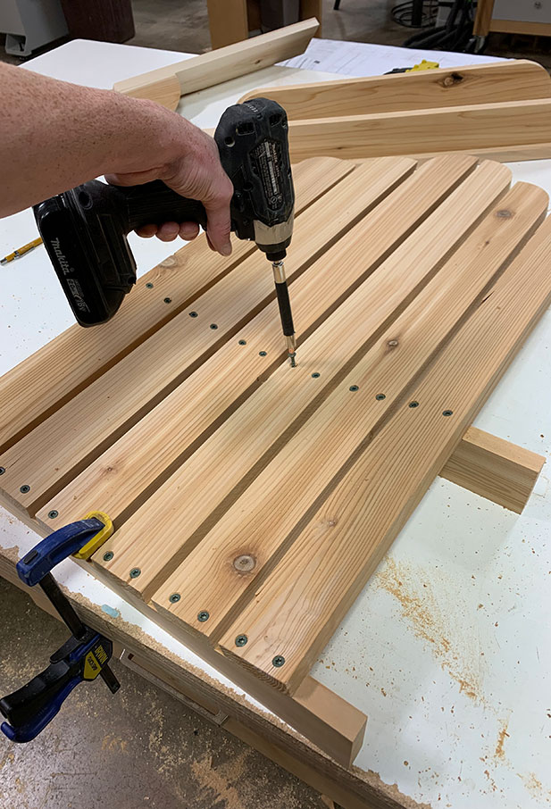 A woodworker attaching back slats to a DIY Adirondack chair project.